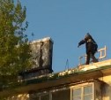 В Охе рабочие без страховки ходят по крыше и бросают доски на дорогу