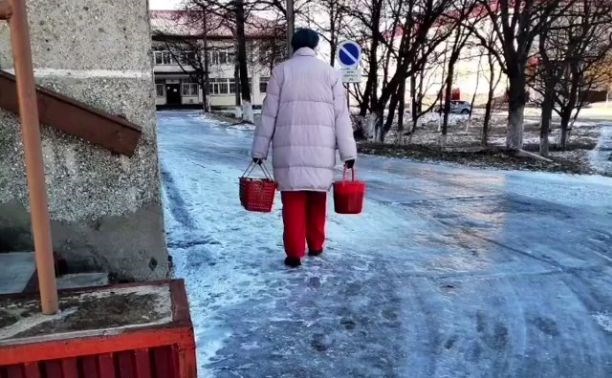 Буфетчицы с вёдрами скользят по ледяной дороге на территории Поронайской ЦРБ